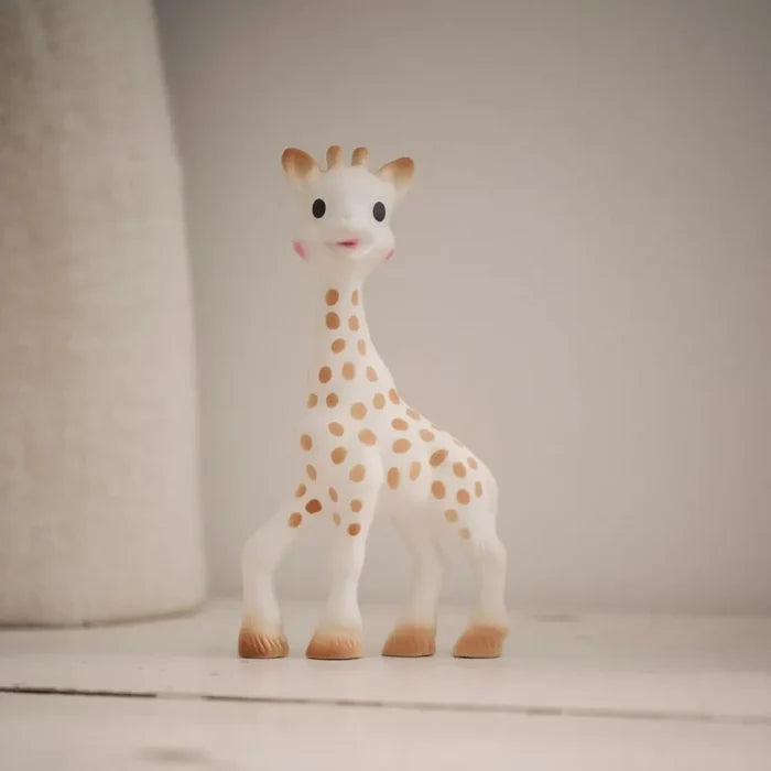 A small white giraffe toy with tan spots stands on a light surface against a soft beige background.