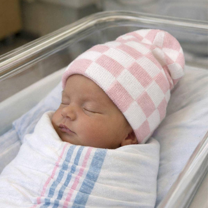 Newborn baby swaddled in a blanket with a pink and white checkered hat in an incubator.