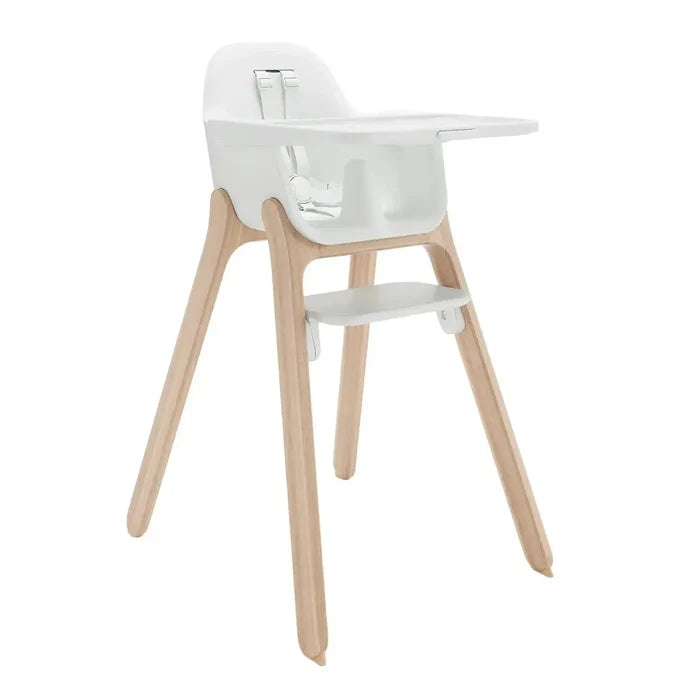 A modern high chair featuring a white molded plastic seat, tray, and footrest, supported by four natural light wood legs, shown against a solid white background.