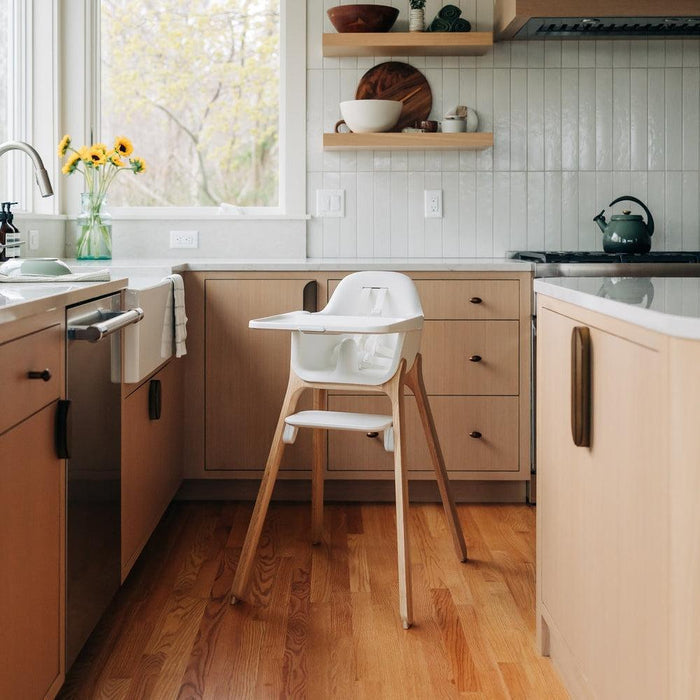 Kitchen with wooden high chair, light-colored cabinets, and a window with yellow flowers.