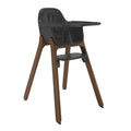 A modern high chair featuring a dark gray molded plastic seat, tray, and footrest, supported by four tapered brown wooden legs, shown against a plain white background.