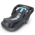 A black UPPAbaby infant car seat extra base designed for Mesa + Mesa V2 models. The image shows the base with a red-to-green tightness indicator and blue seat belt routing.