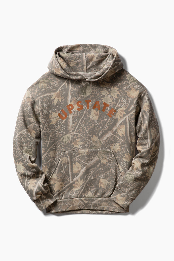 A camouflage hoodie featuring a woodland tree-bark pattern in shades of brown, beige, and gray, with the word 'UPSTATE' printed in orange arched across the chest.
