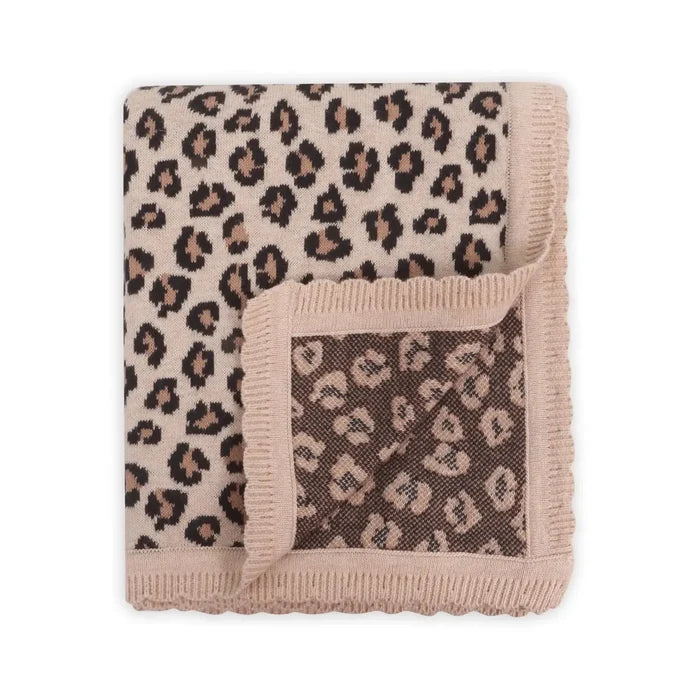 A folded knit blanket with a leopard print pattern in beige, brown, and black, featuring a solid beige fringed border.