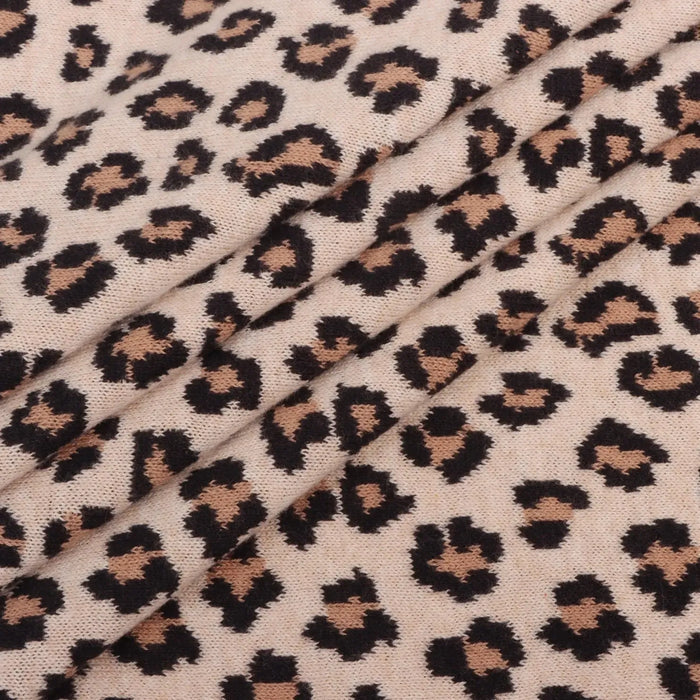 Leopard print knit fabric with black and tan spots on a warm beige background, shown in soft folds.