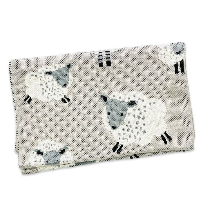 A folded fabric item, likely a blanket or towel, featuring a repeating pattern of stylized white sheep with gray faces and black legs on a light beige textured background.