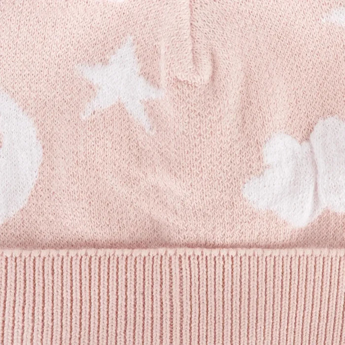 Close-up of a pink knit fabric with white star and cloud motifs and a ribbed hem.