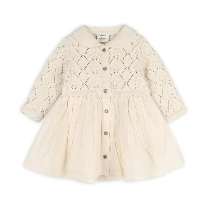 A cream-colored baby dress with a textured knit bodice, long sleeves, and a gathered flared skirt, featuring a button-up front.