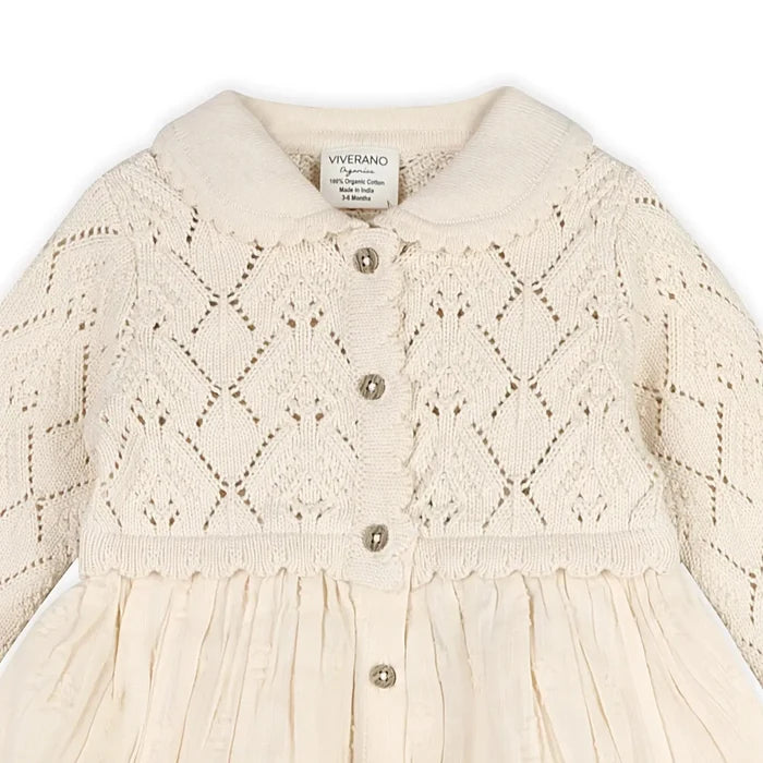 An off-white cream knit baby cardigan dress by Viverano, featuring a diamond-knit pattern on the bodice, a soft collar, and decorative buttons down the front.