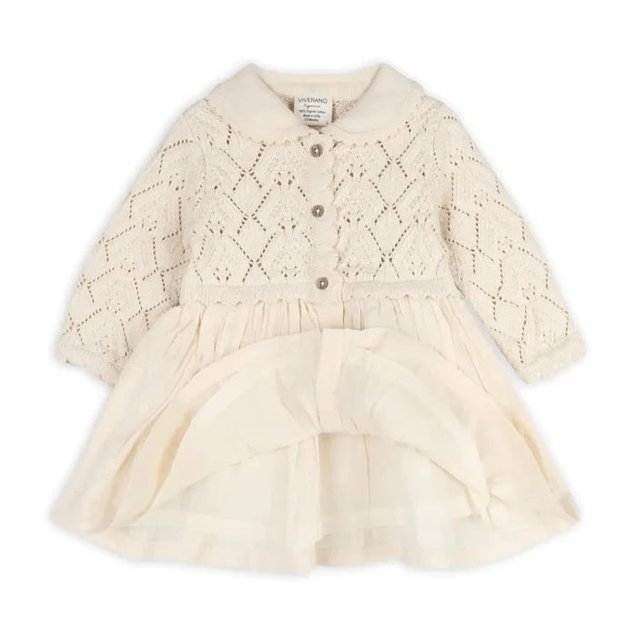 An off-white/cream baby dress with a textured, open-knit cardigan-style bodice featuring three buttons, long sleeves, and a gathered ruffled skirt.