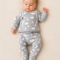 A baby lying on a textured cream blanket, wearing a light gray two-piece sleeper set with a white cloud and moon pattern.