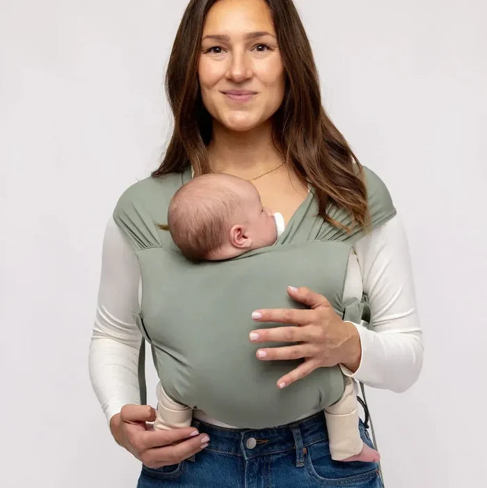 Woman holding a baby in a green baby carrier against a white background