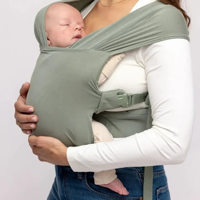 Person holding a baby in a green baby carrier against a plain background