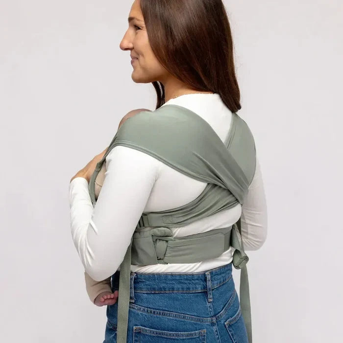 Woman wearing a green baby carrier on a plain background