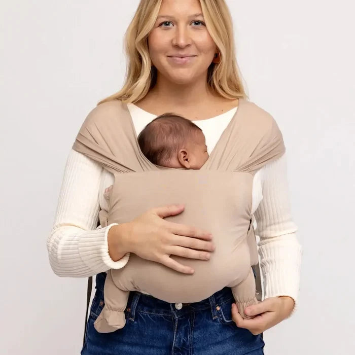 Woman holding a baby in a beige baby carrier against a white background
