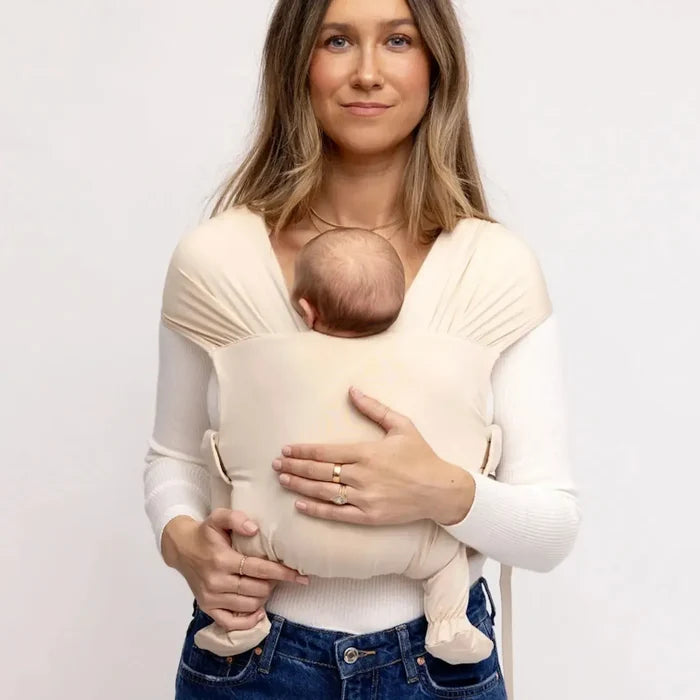 Woman holding a baby in a sling against a plain background