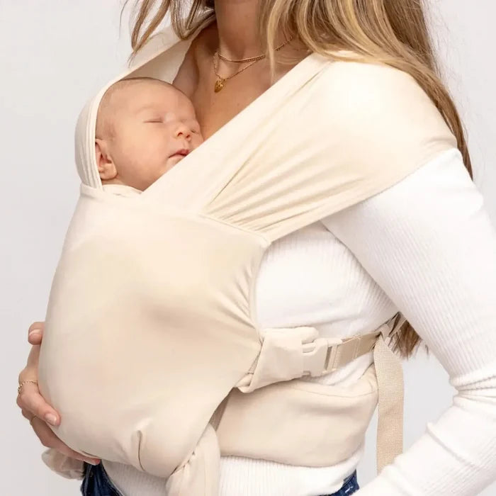 Woman holding a baby in a cream baby carrier against a white background