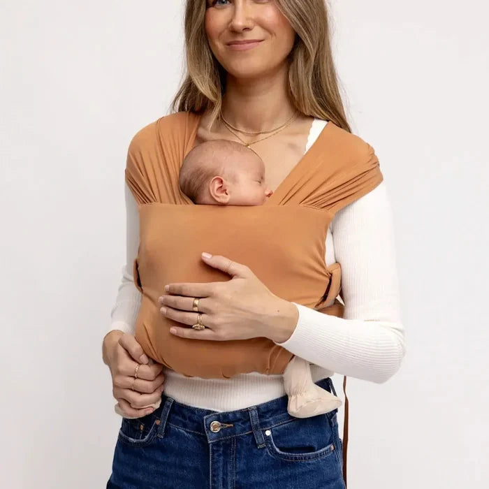 Woman holding a baby in a sling against a plain background
