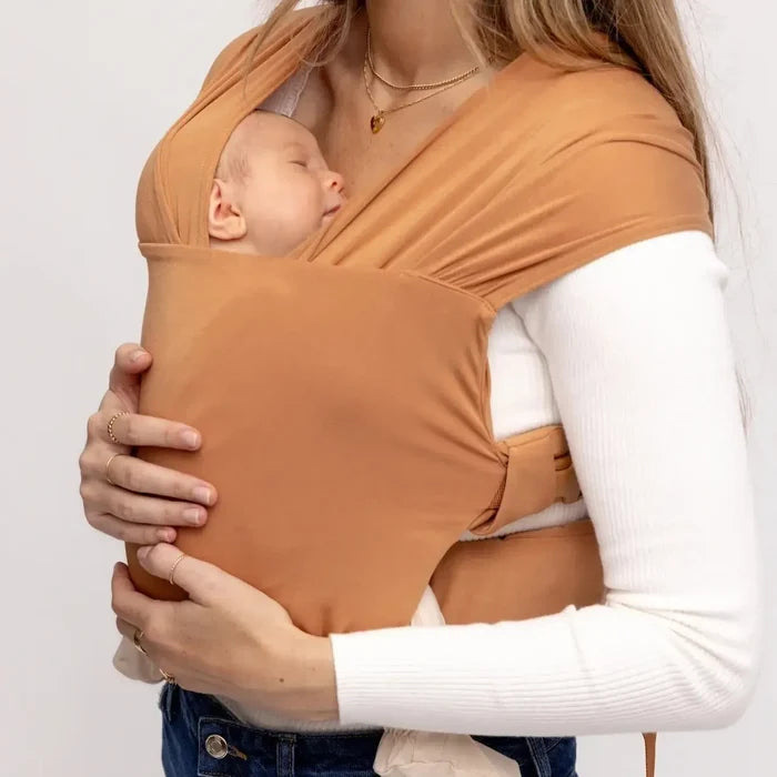 Person holding a baby in an orange baby carrier against a white background