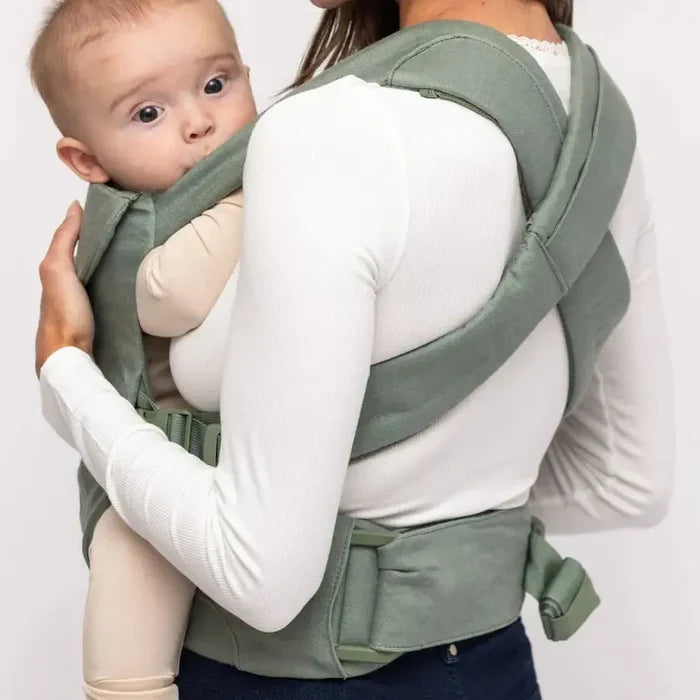 Woman carrying a baby in a green baby carrier against a white background