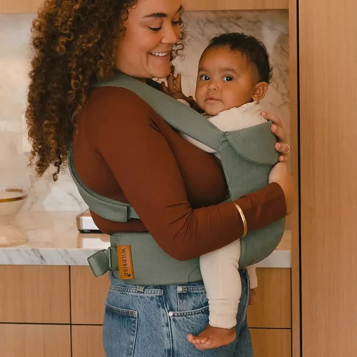Woman holding a baby in a carrier in a kitchen setting