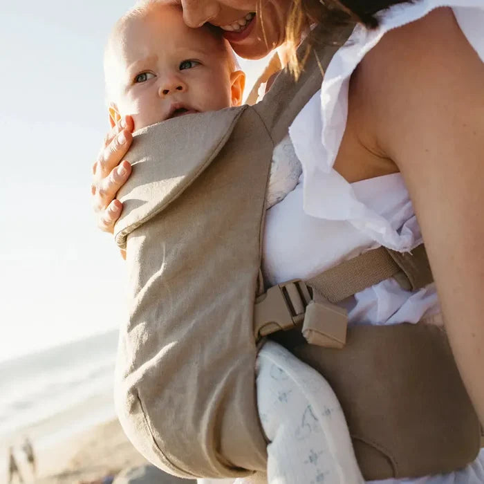 Woman holding a baby in a carrier on a beach