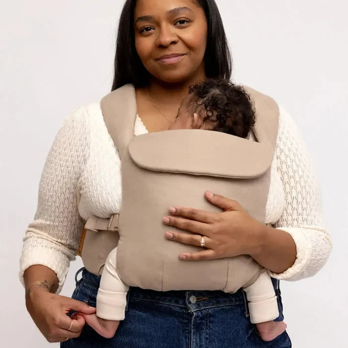 Woman holding a baby in a beige carrier against a white background