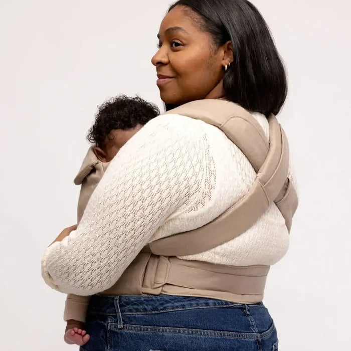 Woman carrying a child using a baby carrier on a plain background