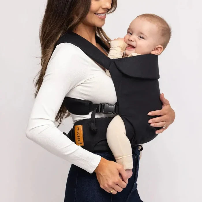 Woman holding a baby in a black baby carrier against a white background