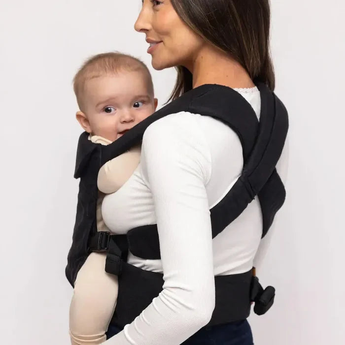 Woman carrying a baby in a black baby carrier against a white background