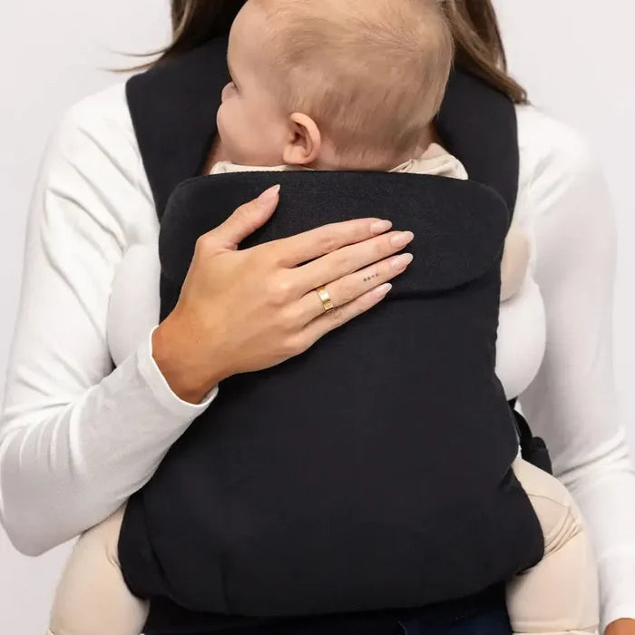 Woman holding a baby in a black carrier against a white background