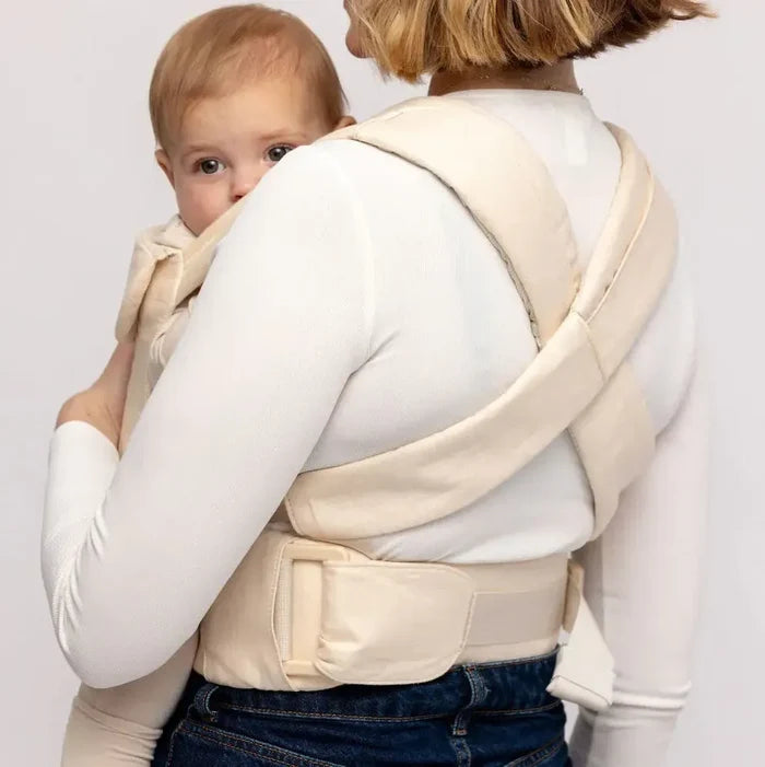 Woman wearing a baby in a cream carrier against a white background
