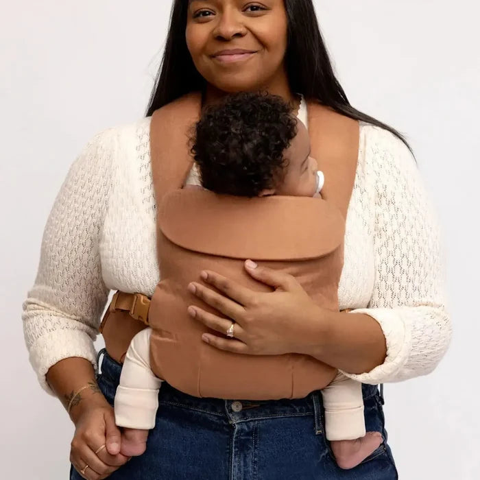 Woman holding a baby in a brown baby carrier against a white background