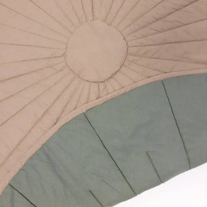 Close-up of a quilted fabric item, likely a blanket or comforter, featuring a sunburst pattern in light beige and a pleated lower section in muted sage green.
